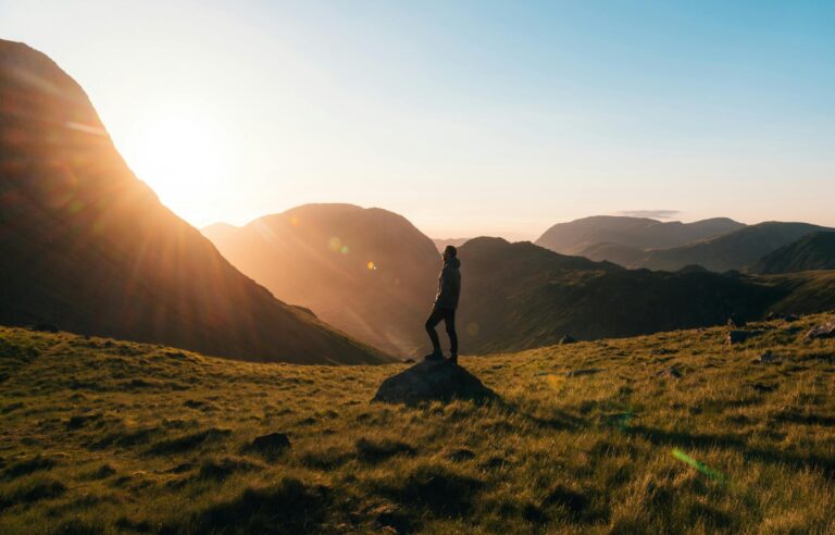 Silhouette of a person standing on a hill during sunrise in Cumbria, England with scenic mountain views.